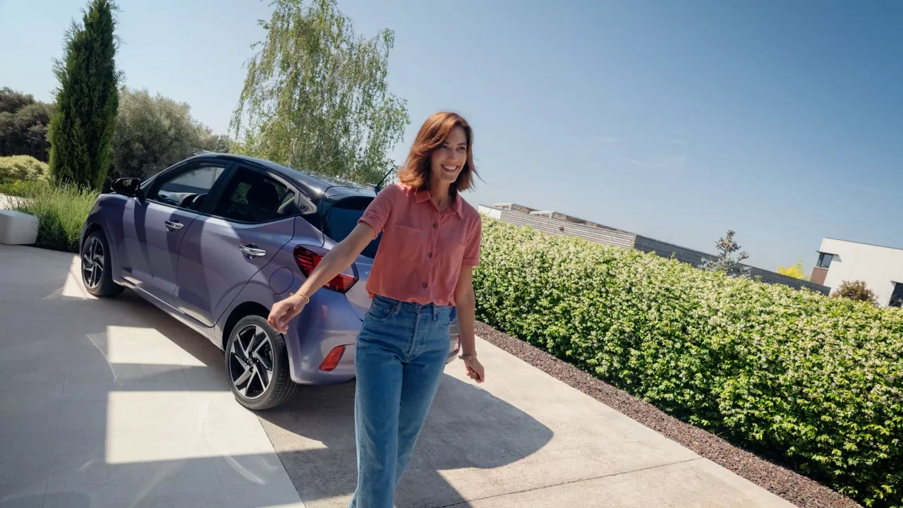 Une femme marchant derrière la nouvelle Hyundai i10 sous le soleil.